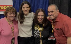 Lynn and her friend Barb posing with Jennifer Carpenter and David Zayas at Steel City Con, all four smiling with convention lanyards and a blue curtain backdrop.
