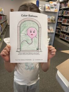 A child holds up a completed Color Balloon activity sheet from The Hallway of Doorknobs activity book at the Tyrone-Snyder Public Library.